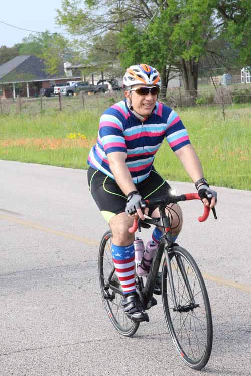 Colorful cyclist riding on rural road for Bluebonnet Express event.