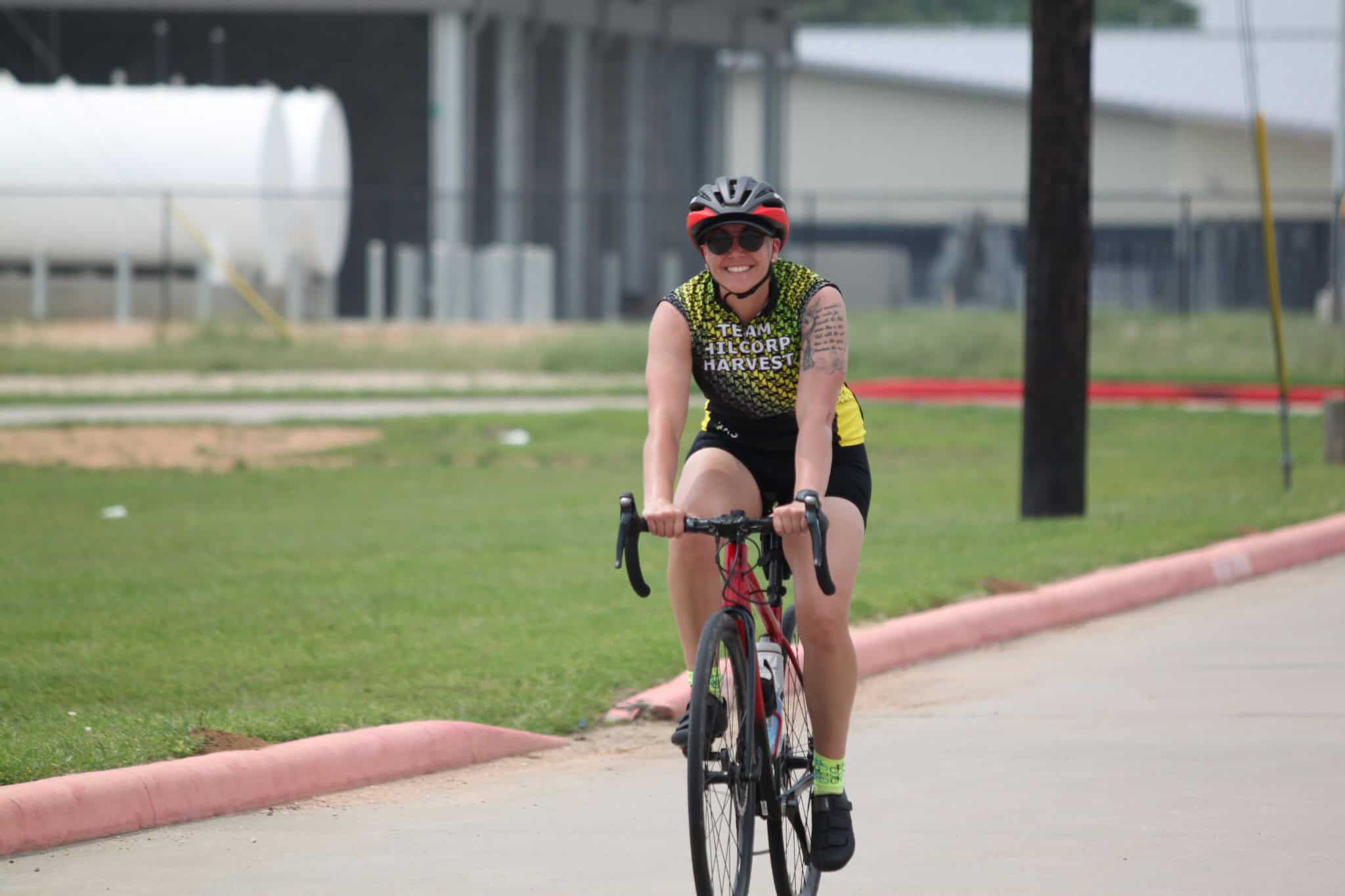 Bright smiling woman riding a bike on a sunny day, sportswear, helmet, and sunglasses, outdoor cycling, Bluebonnet Express.