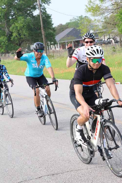 Bright cyclists riding on the scenic Bluebonnet Express route in Texas, enjoying a group ride with smiles and waving excitement.