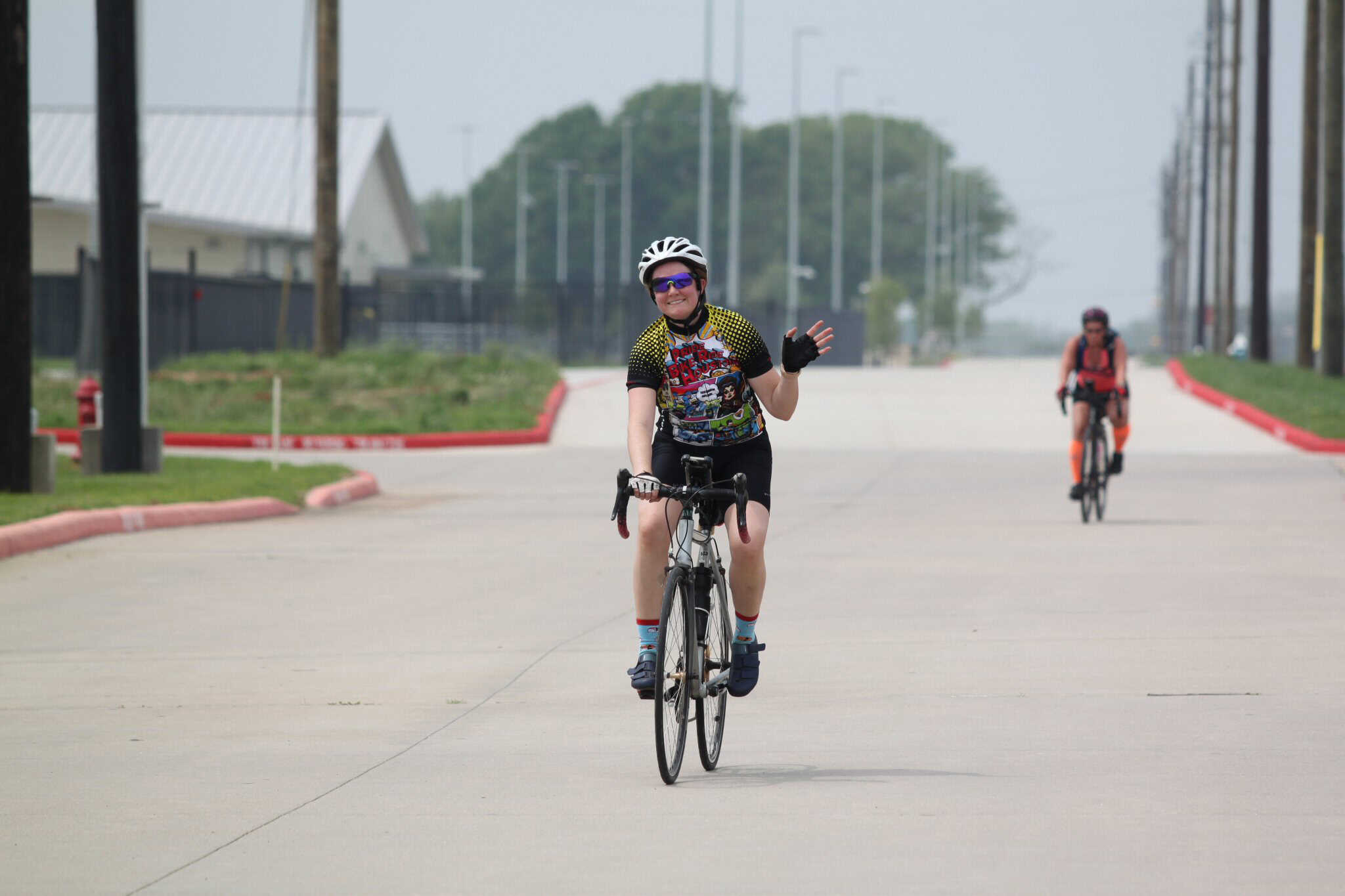 Vibrant woman cyclist smiling and waving during Bluebonnet Express ride, enjoying outdoor biking event.