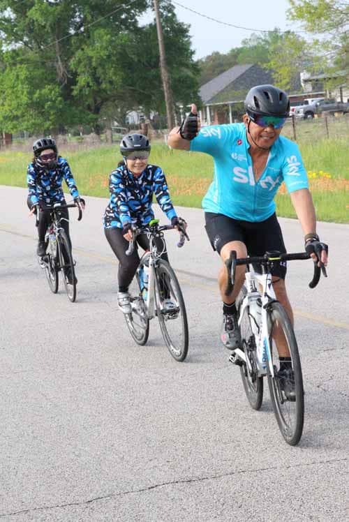 Cyclist celebrating with children riding bikes on a rural road during a group cycling event.