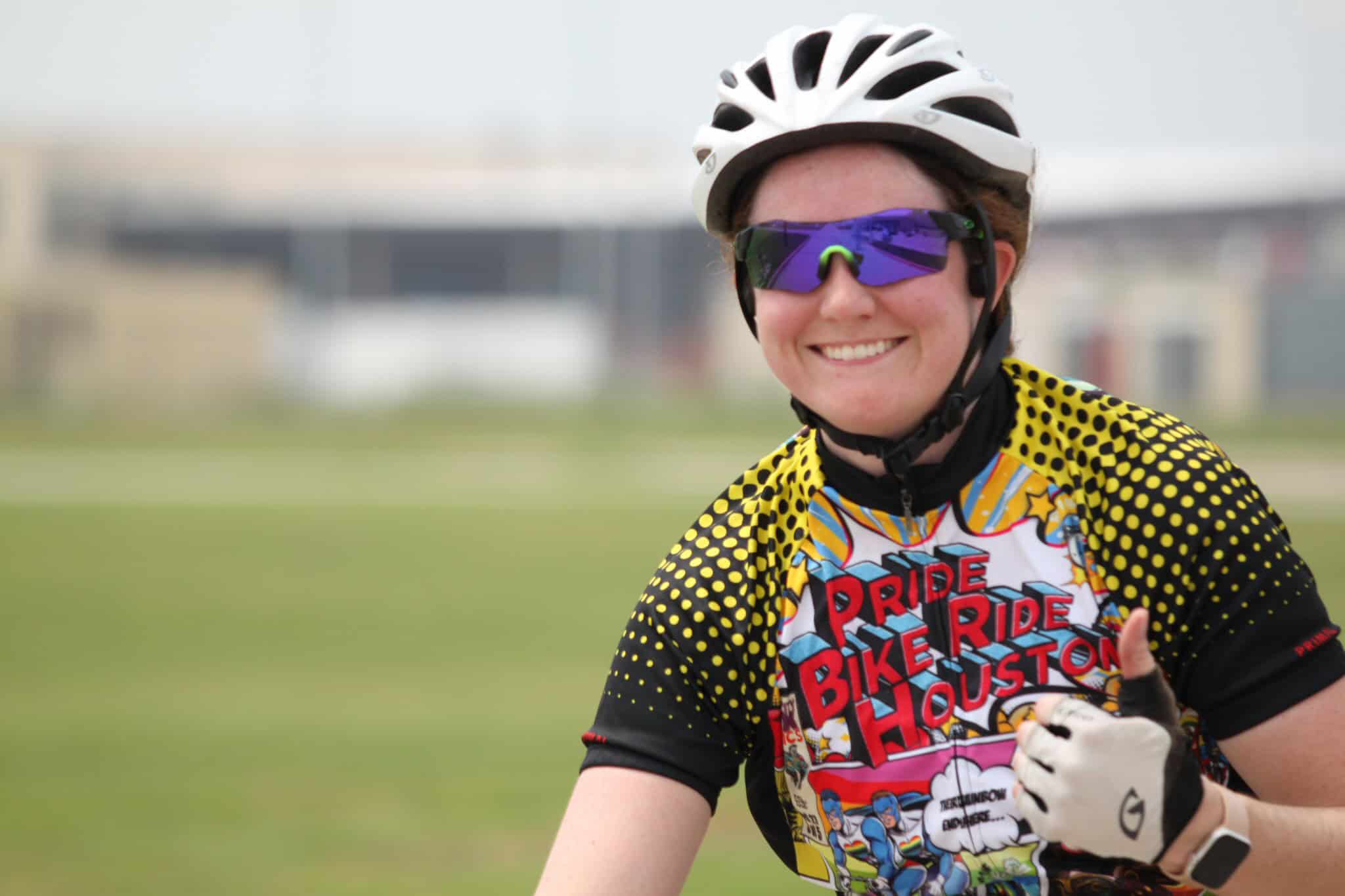 Colorful cyclist in Houston Pride Bike Ride jersey, smiling with helmet and sunglasses outdoors.