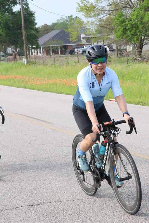 Comfortable blue and black road cycling bike outdoors, woman smiling, wearing helmet and sunglasses.
