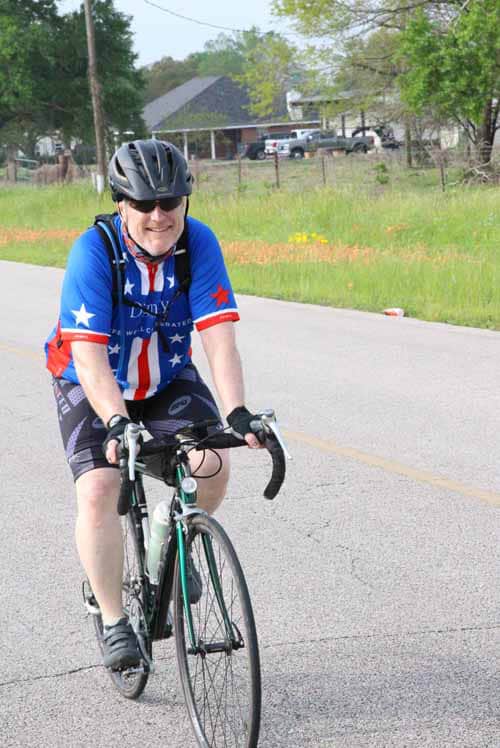 Bright-eyed cyclist wearing patriotic gear riding on a scenic road during Bluebonnet Express event.