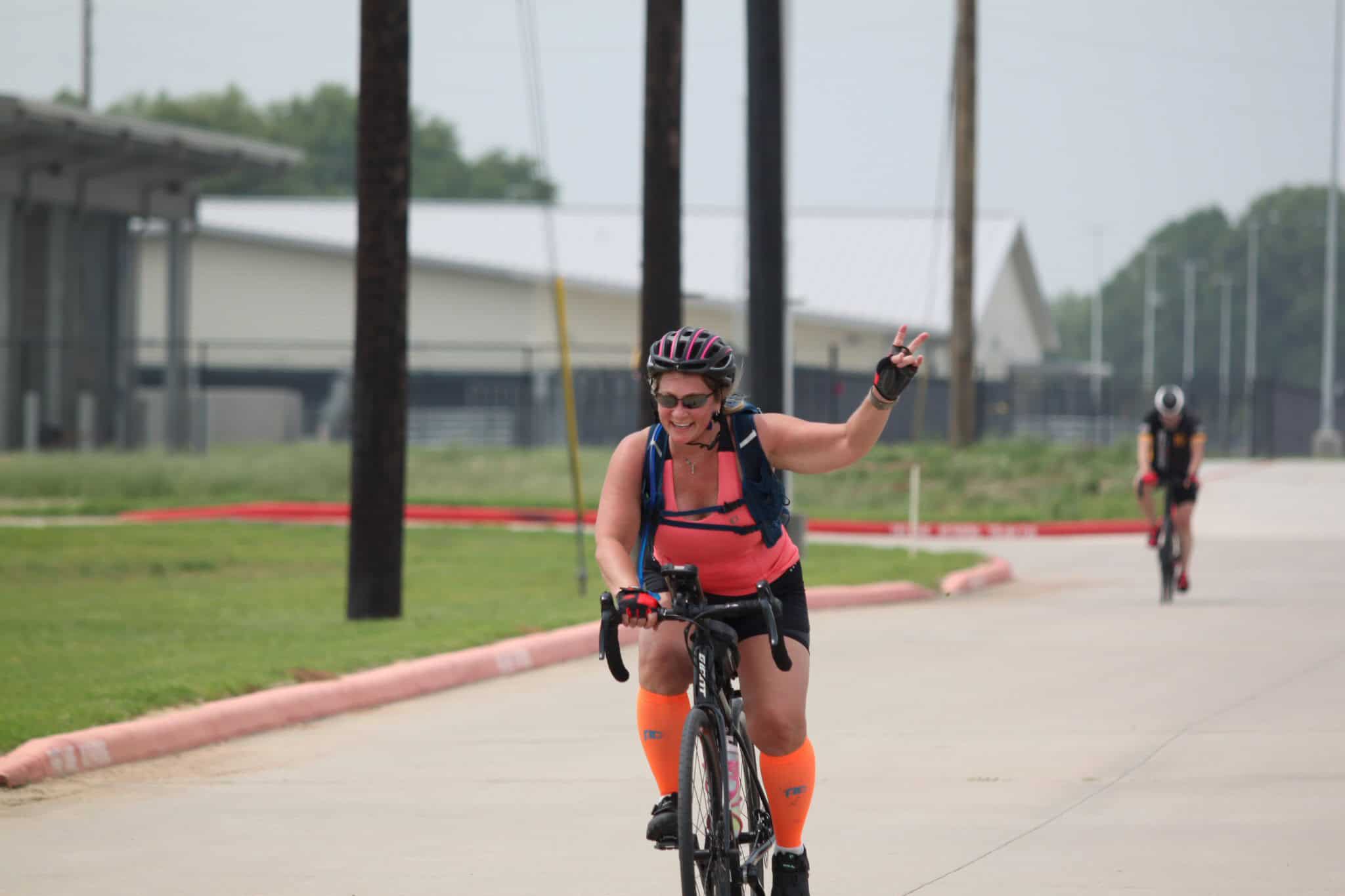 Vibrant woman cyclist enjoying Bluebonnet Express trail, making peace sign during bike ride.
