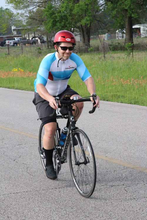 Bright cyclist riding on road in Bluebonnet Express cycling jersey, enjoying outdoor bike ride.