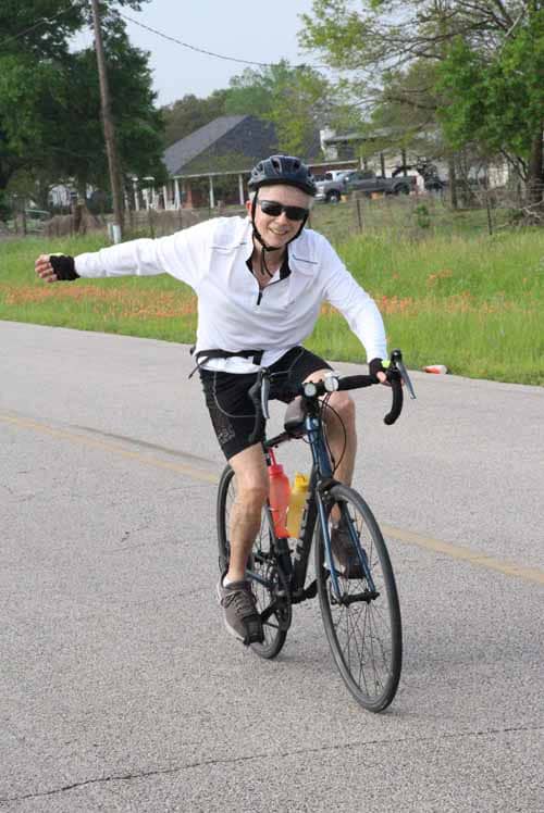 Smiling cyclist enjoying a ride on a scenic Greenway trail with Bluebonnet Express bike route signage.
