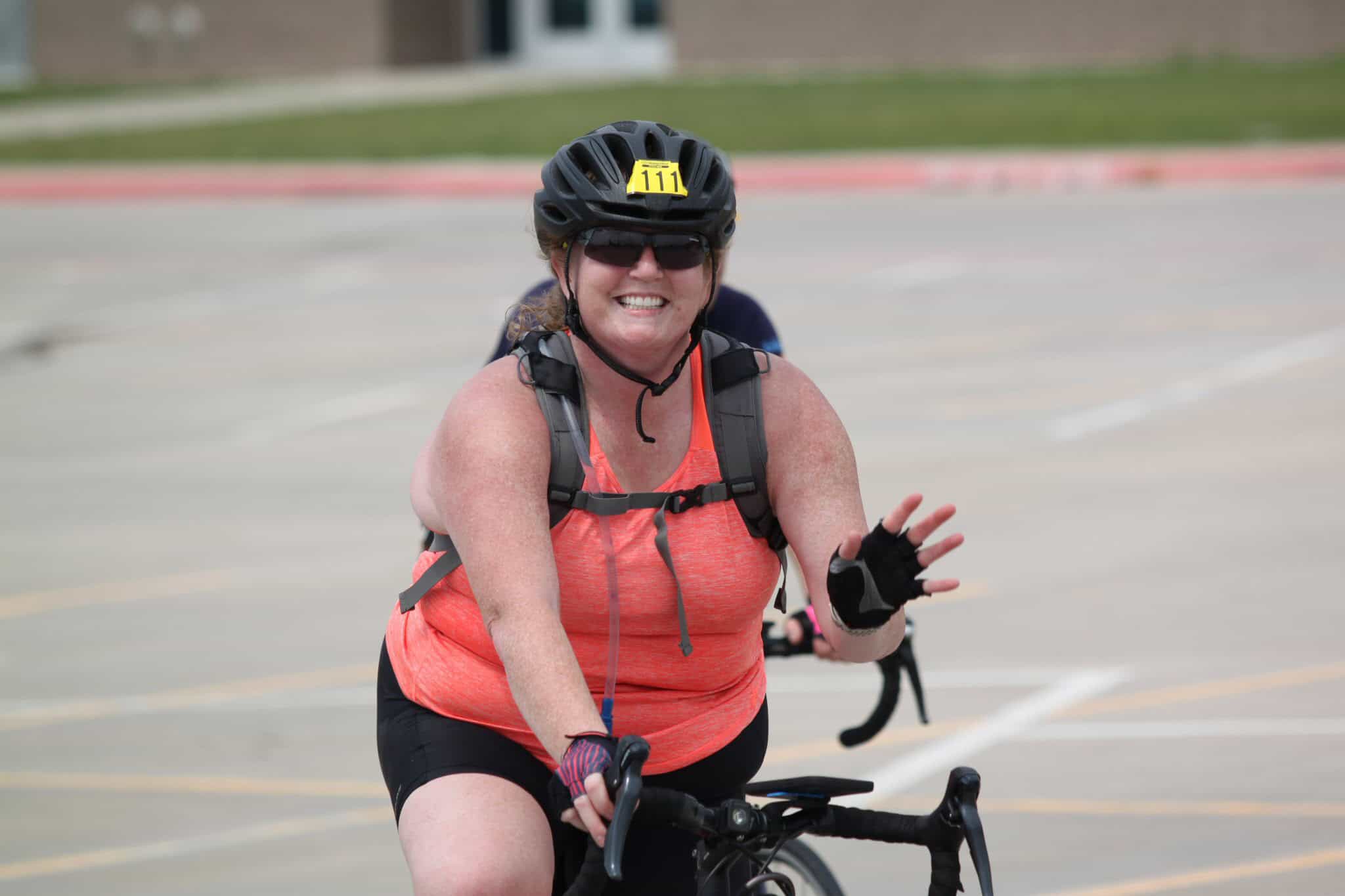 Bright smiling woman cyclist wearing helmet and sunglasses, participating in Bluebonnet Express bike event.