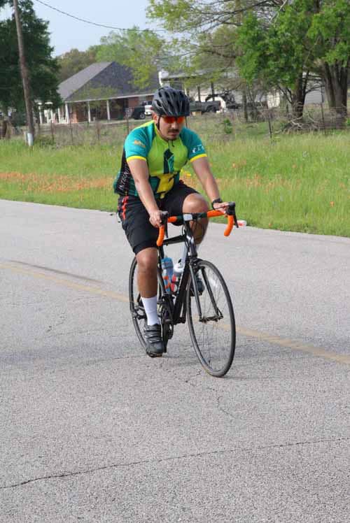 Bright cyclist riding on a rural road during daytime, promoting Bluebonnet Express bike services.