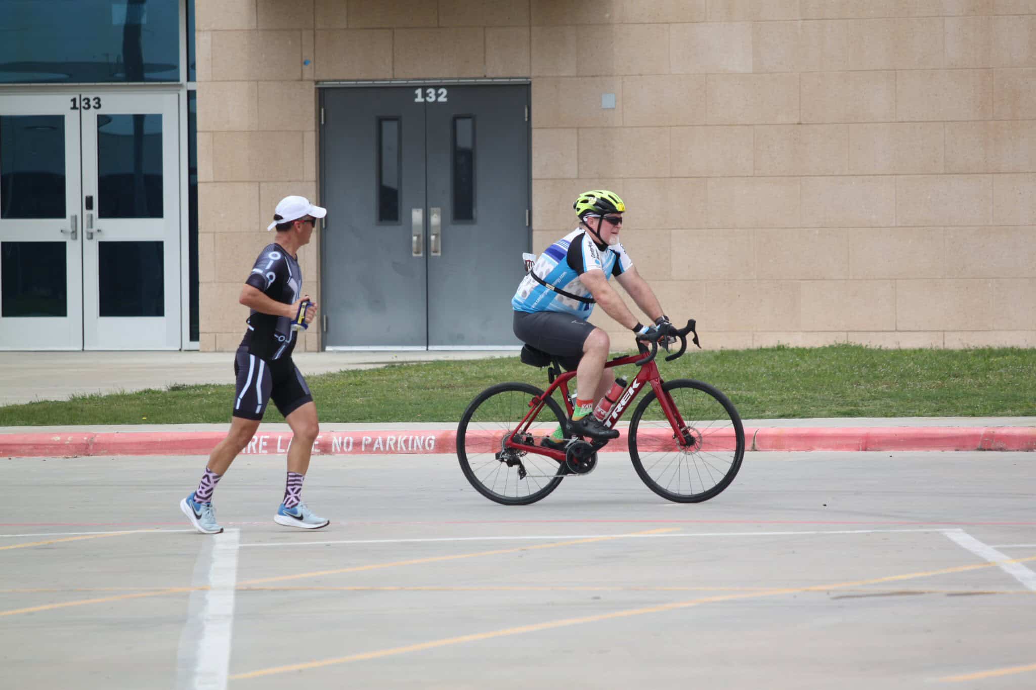 Cyclist wearing Bluebonnet Express gear riding on street with a runner nearby.