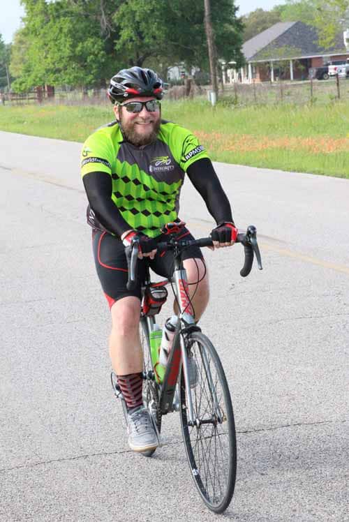 Bright green and black cyclist jersey on smiling man riding bike on open road outdoors.