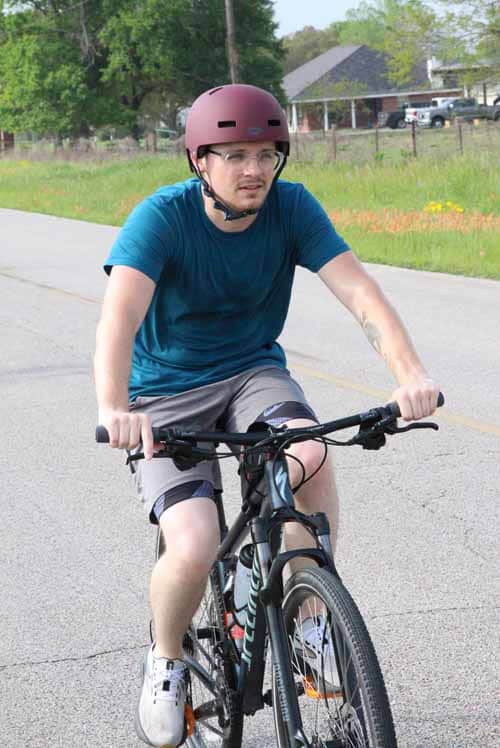 Bright blue helmet and shirt on male cyclist riding mountain bike on suburban street during daytime.