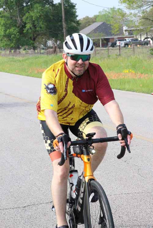 Velo rider in yellow and maroon jersey cycling on rural road during daytime.