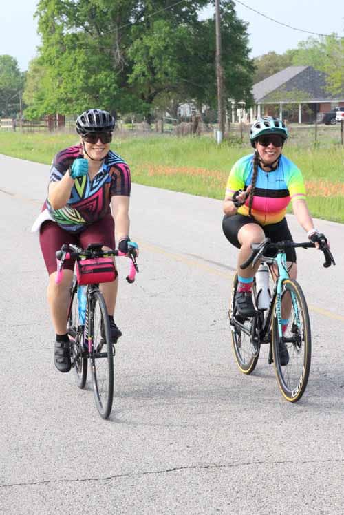 Brightly colored women cycling together on a scenic rural road during daytime.