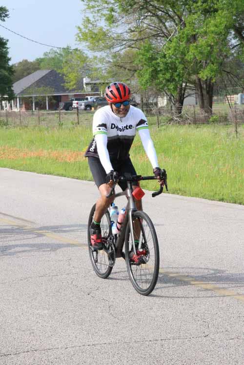 Bright cyclist riding a black road bike on a suburban street during daytime.