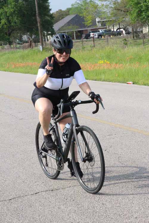 - Smiling cyclist wearing helmet making peace sign during daytime ride on Bluebonnet Express.