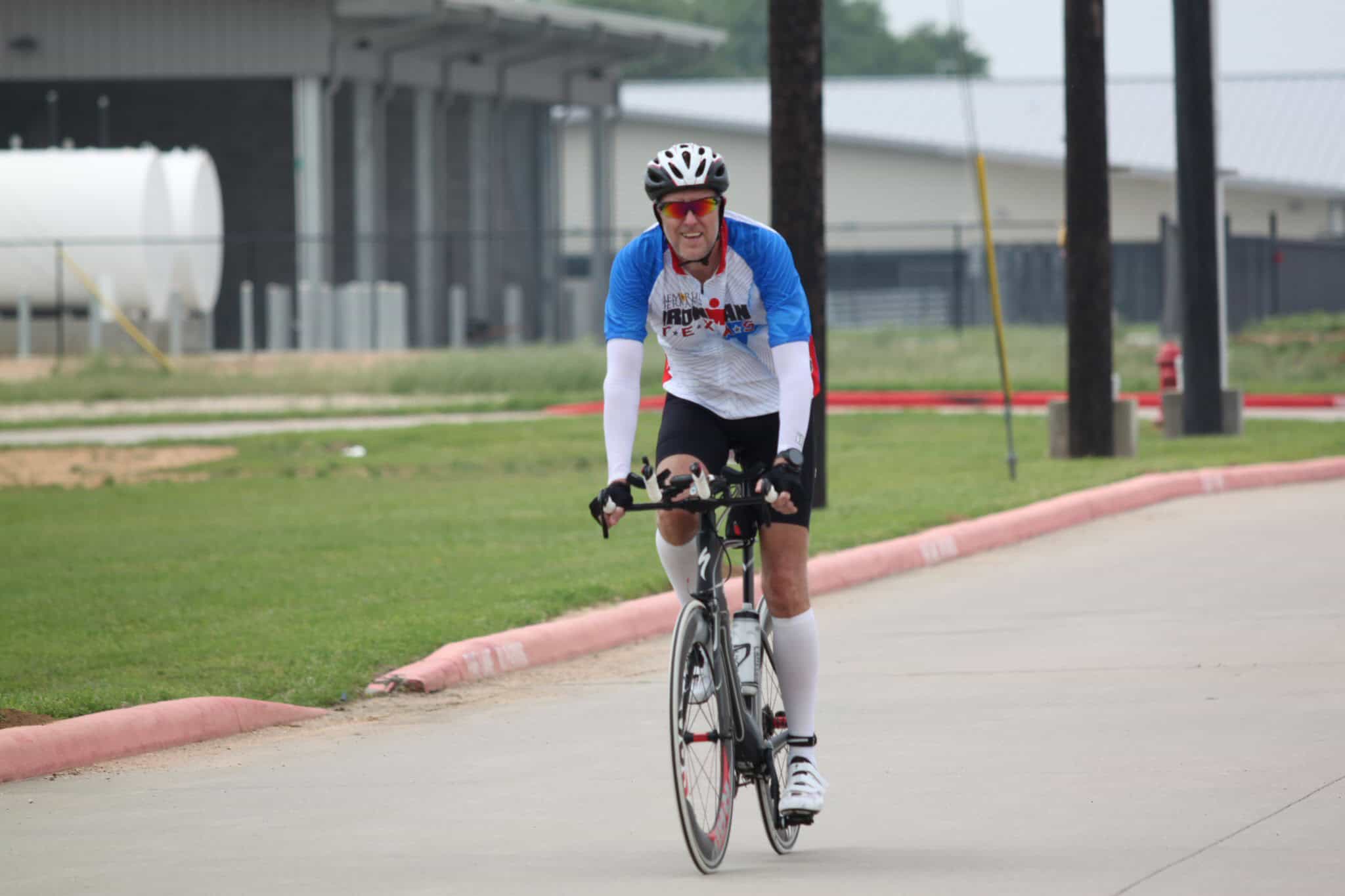 Cyclist riding on a paved road wearing a Bluebonnet Express jersey and safety helmet for outdoor biking.