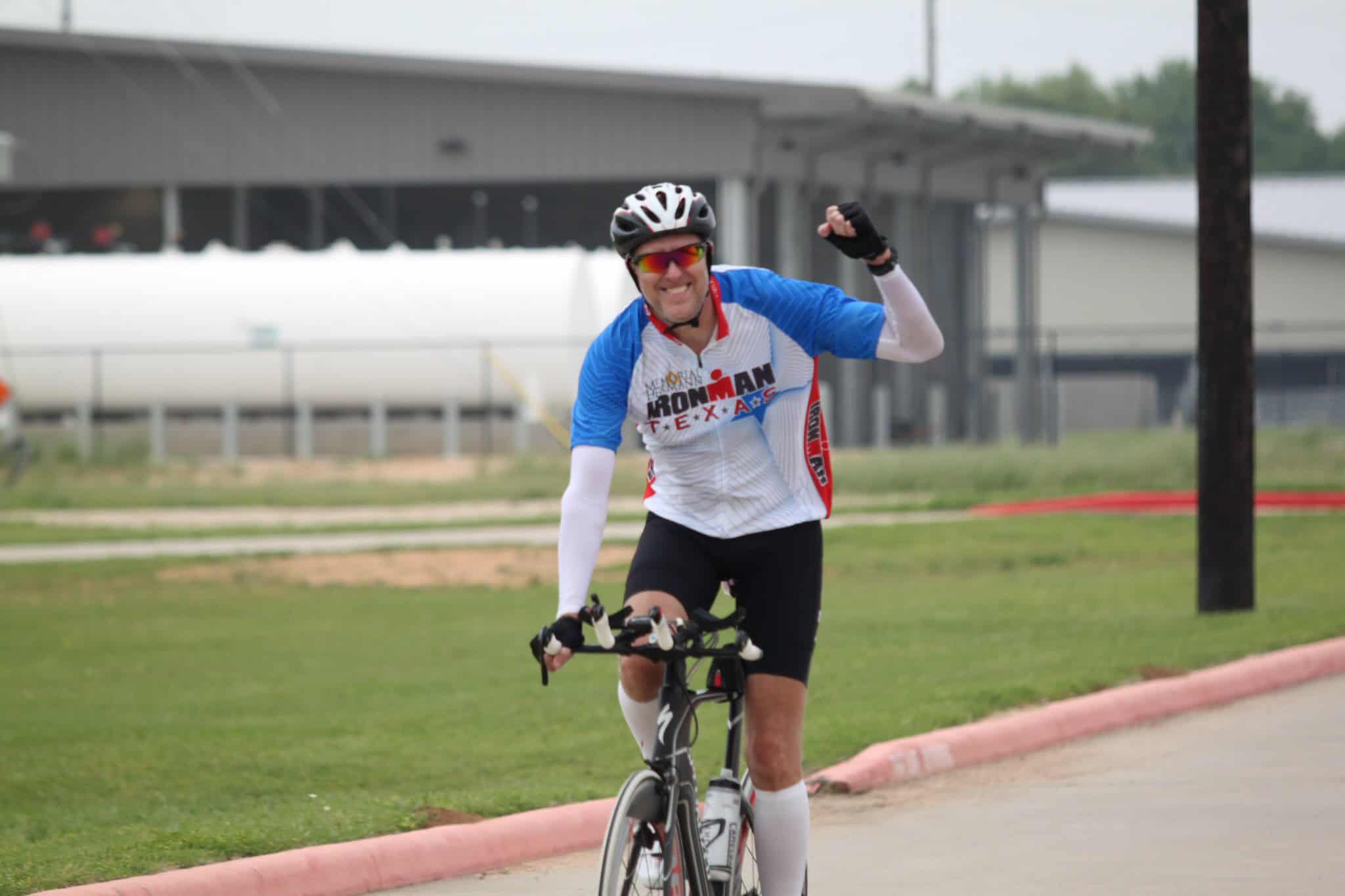 Bright male cyclist riding a bike during Bluebonnet Express event, wearing professional cycling gear and helmet, smiling after race.