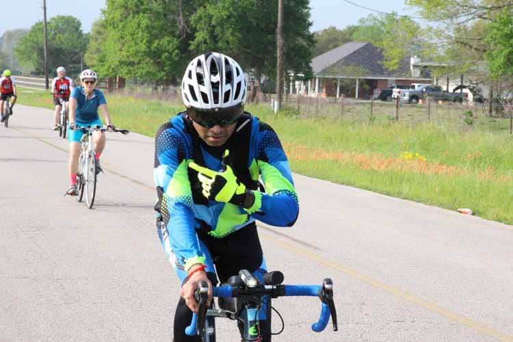 Bike rider in blue and neon gear with group cycling on rural road during Bluebonnet Express event.