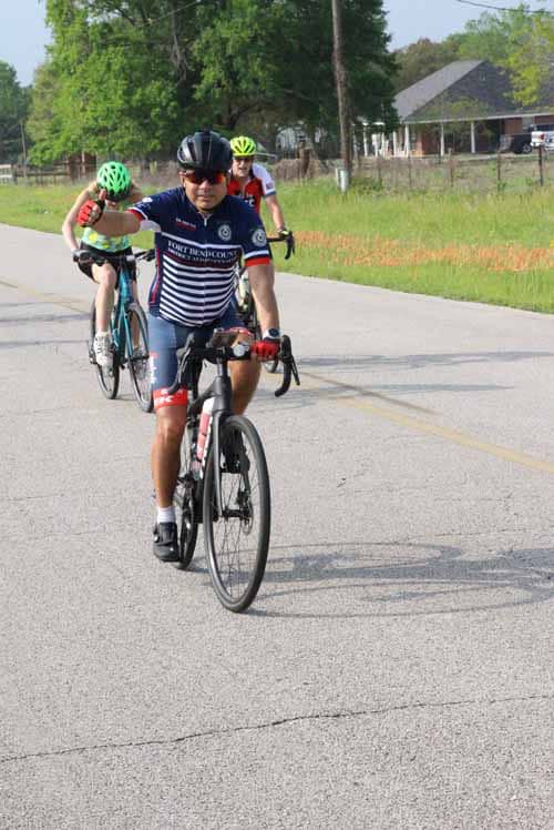 Brightly dressed cyclists ride along a scenic road during Bluebonnet Express event.