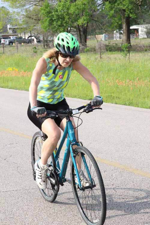 Woman riding a blue bike on a rural road during daytime, protecting her head with a helmet.
