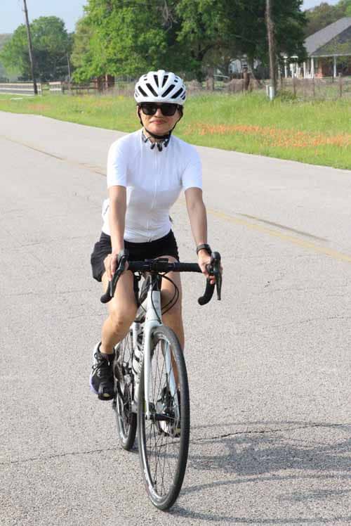 Female cyclist riding a bike on a suburban street in a white helmet and cycling gear.