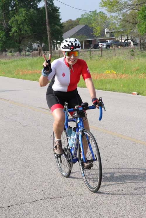 Vegan cyclist riding a Bluebonnet Express bike and making a peace sign outdoors in spring.