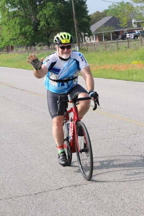Bright male cyclist waving on the road during outdoor biking event.