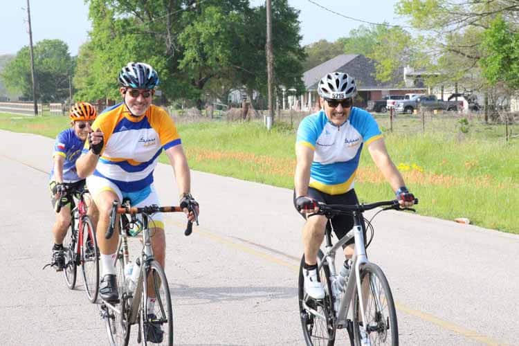 Bright group of cyclists riding on a sunny rural road, enjoying a casual bike ride with helmets and sporty attire.