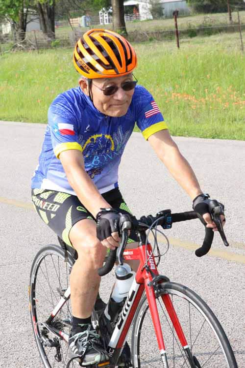 Bright elderly cyclist riding a bike wearing a helmet and sports gear on a sunny day.