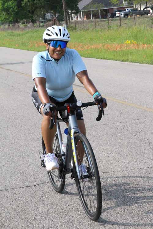 - Woman cycling on road wearing helmet and sunglasses, Bluebonnet Express.