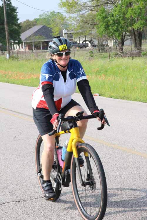 Active woman riding a yellow bicycle during Bluebonnet Express event, outdoors in a rural setting.