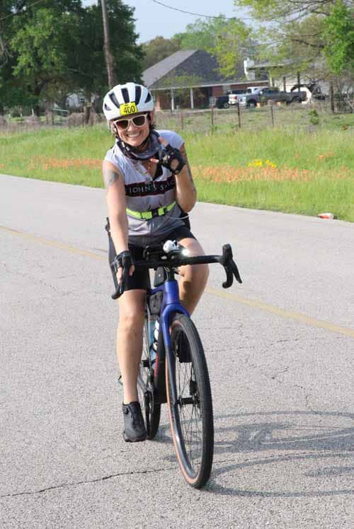 Bright female cyclist riding on the Bluebonnet Express bike trail with a helmet and sunglasses.