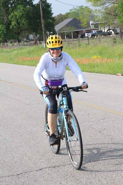 Bright woman cycling on a scenic road wearing a yellow helmet and sporty attire.