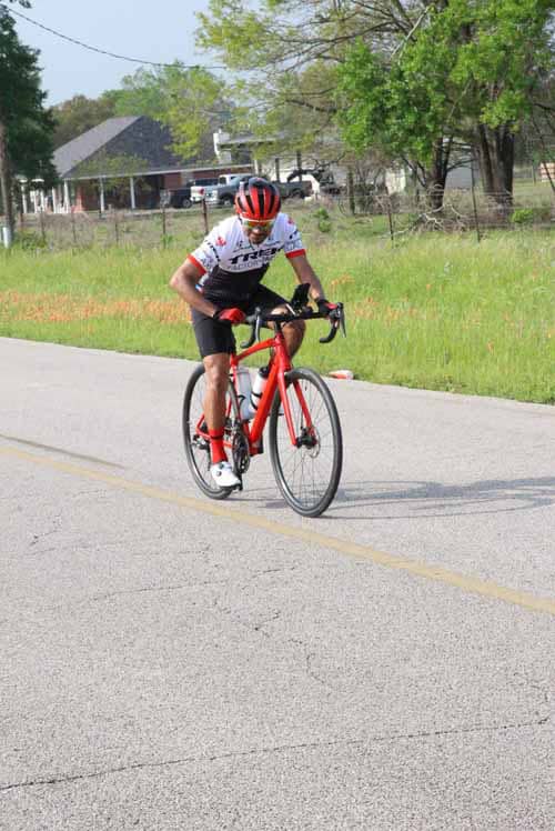 Bright red road bike being ridden on open road by cyclist wearing helmet and sportswear.