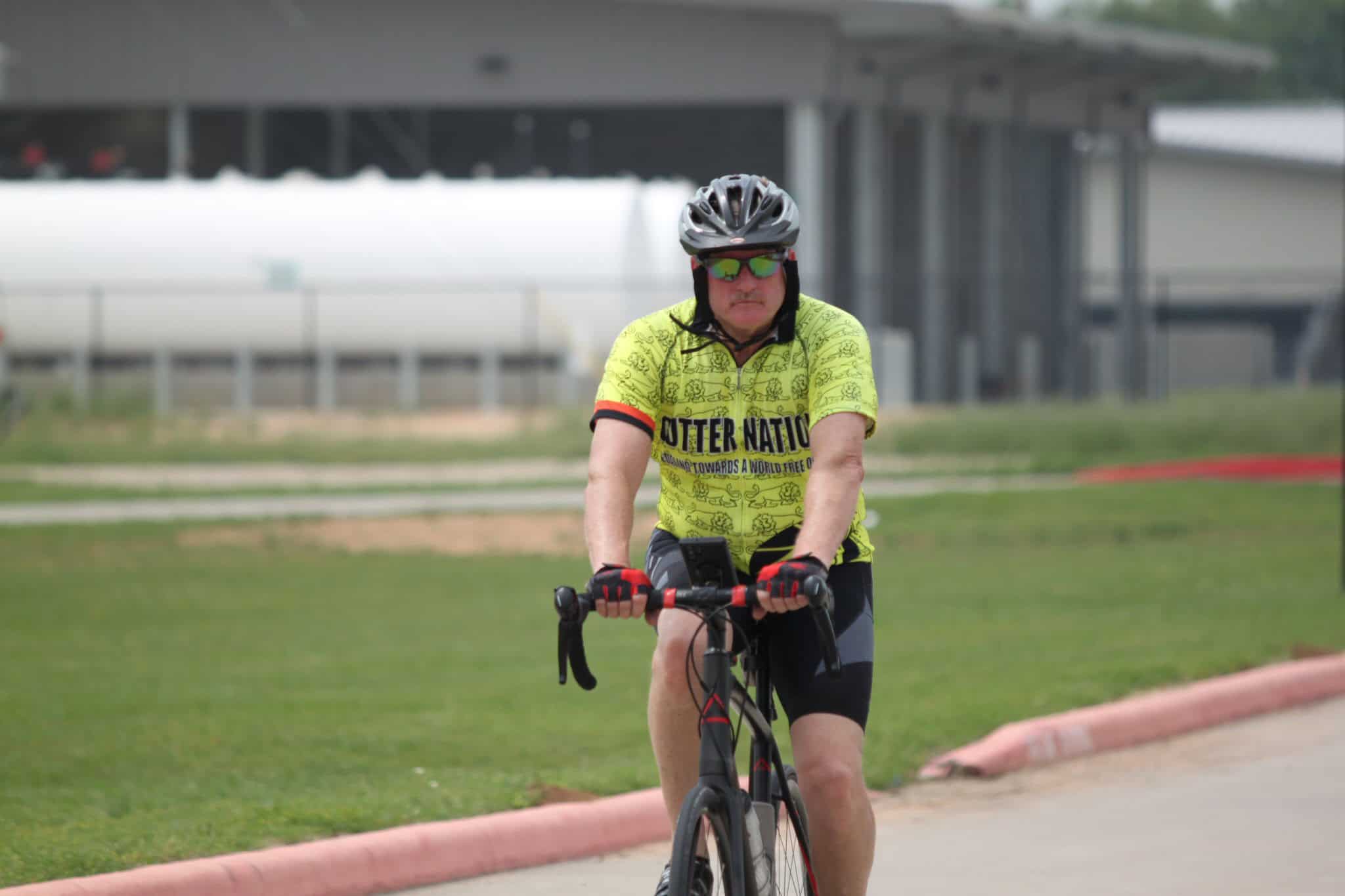 Bright green cyclist jersey with "Outer Nation" text on a mountain bike in outdoor park SEO content: ALT: Man cycling in bright yellow jersey, outdoor park. Caption: Cyclist enjoying a ride in outdoor park with vibrant jersey and gear. Description: Man riding a mountain bike in a green outdoor park, wearing a yellow jersey and helmet, showcasing outdoor cycling adventure.