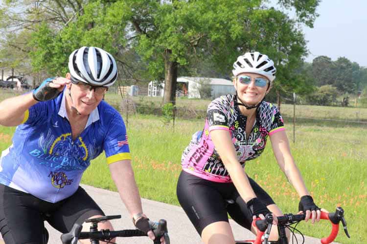 Vibrant Bluebonnet Express cycling team riding in a scenic rural area with green trees and open fields.
