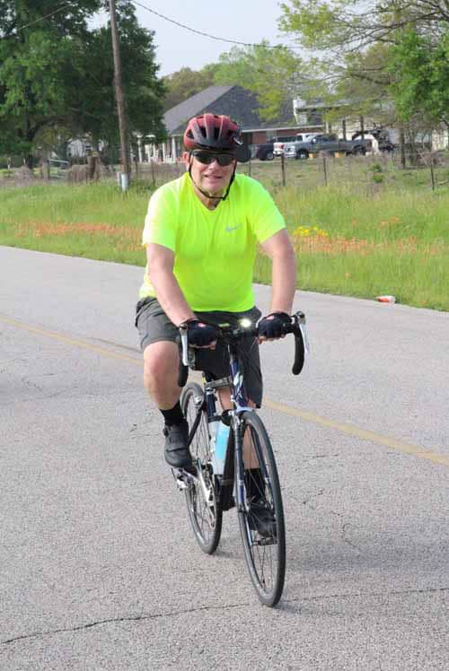 High-visibility cyclist riding on rural road during daytime, eco-friendly transportation, Bluebonnet Express biking event.
