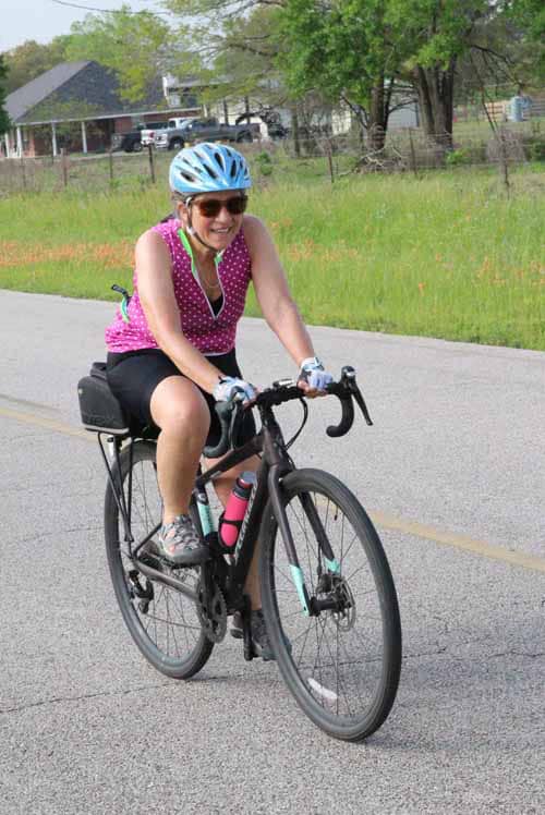 Bright woman cycling on rural road, enjoying outdoor fitness, healthy lifestyle, and biking adventure.