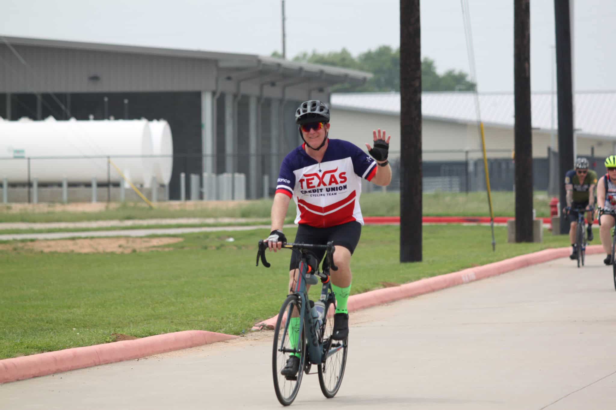 1. Bicycle rider in Texas Texas Cycling Team jersey on a bike, smiling and waving.