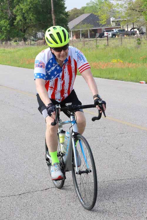 Brightly dressed cyclist in patriotic American-themed jersey riding on open road during Bluebonnet Express event.