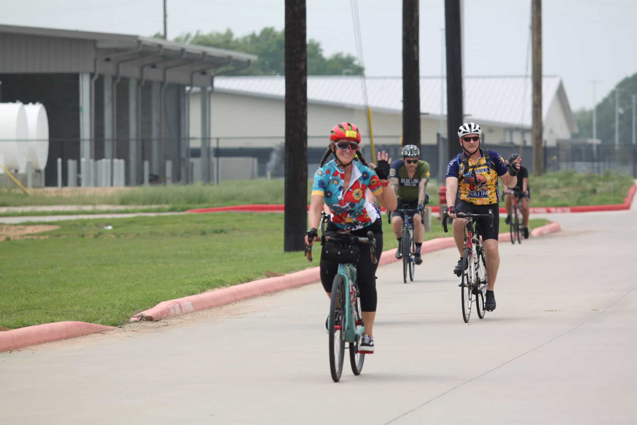 Colorful cyclists riding along a paved path in a suburban area with "Bluebonnet Express" branding in the background.