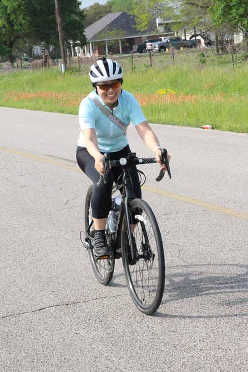 Bright woman riding a bike on a sunny street, promoting wellness and outdoor activities with Bluebonnet Express.