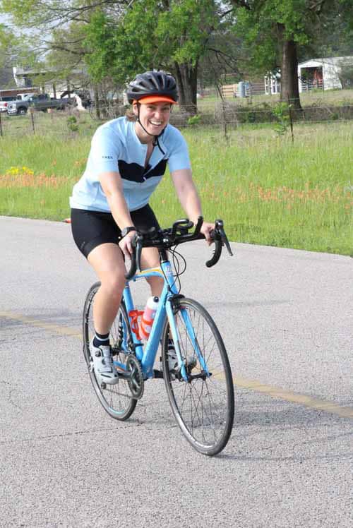 Smiling cyclist riding Bluebonnet Express bike on the road during daytime.