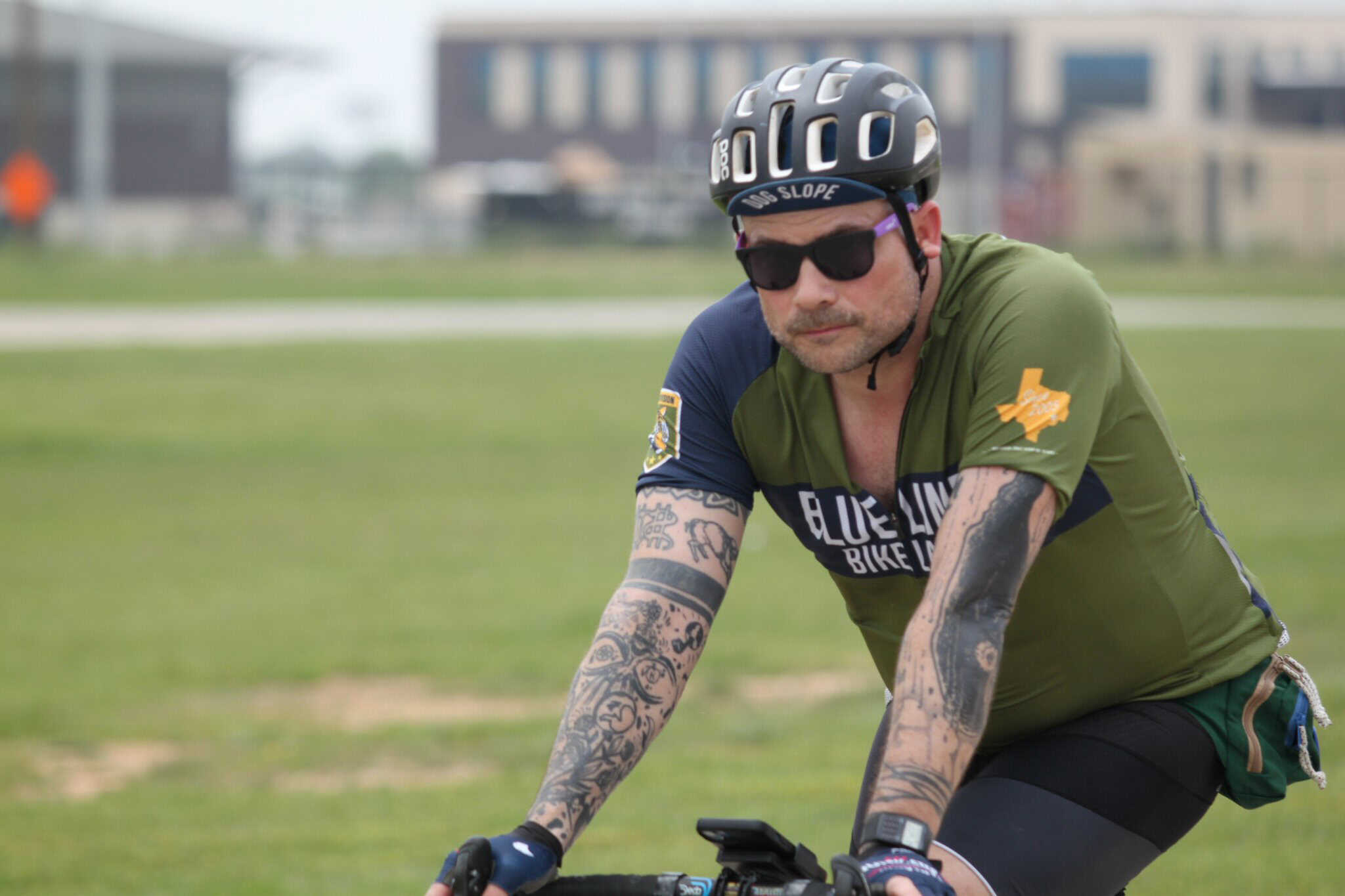 Bold bluebonnet express cyclist riding on grassy field in Texas, wearing helmet and sunglasses.