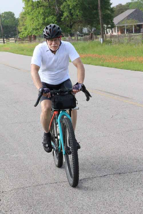A man riding a blue electric bike on a paved road during daytime.
