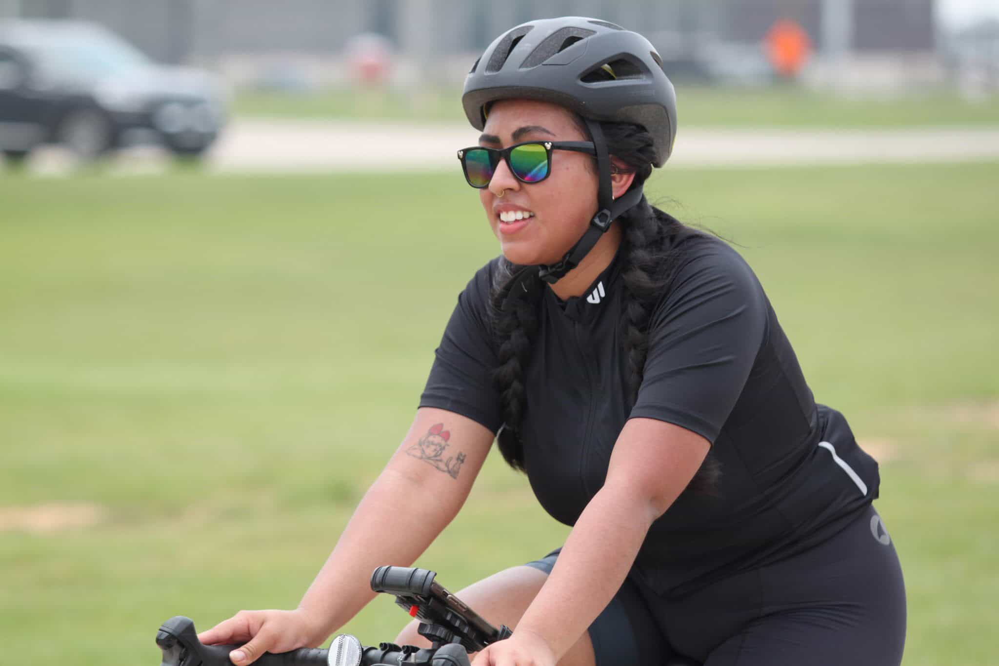 Woman cyclist wearing helmet and sunglasses riding on a bike in a park.