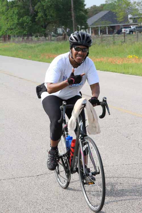 Cyclist riding on open road, wearing helmet and sunglasses, promoting outdoor biking activities.