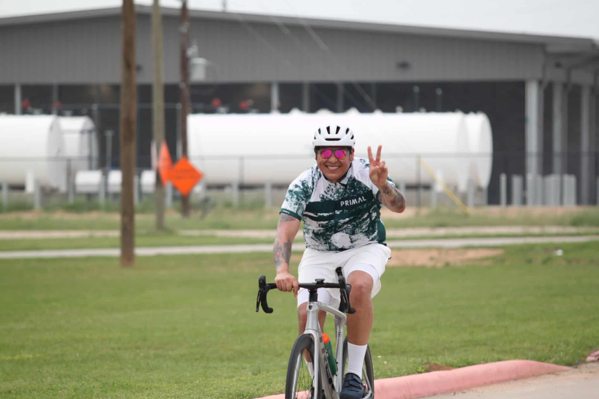 Vegan woman riding bike, making peace sign, smiling outdoors at Bluebonnet Express.