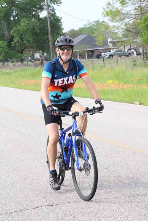 Bright cyclist wearing Texas jersey riding Bluebonnet Express bike on open road during daytime.